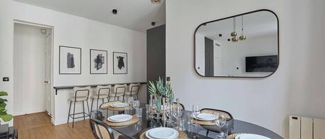 Un coin repas avec une table en verre dressée pour six personnes, entourée de chaises agrémentées de sets de table en fibres tressées.