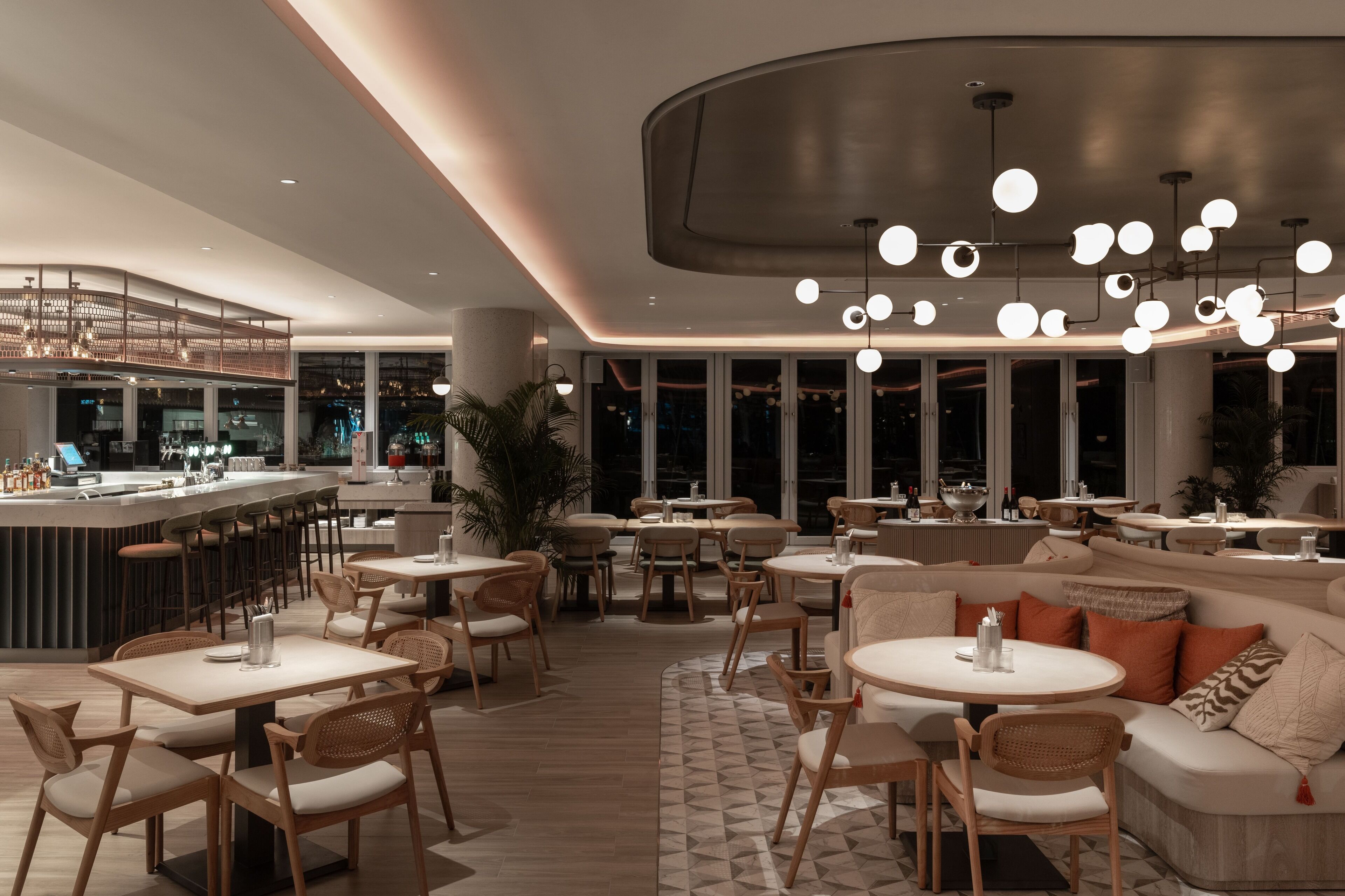Un restaurante moderno con barra, mesas redondas y un espacio de estar acogedor con sofás y sillas.