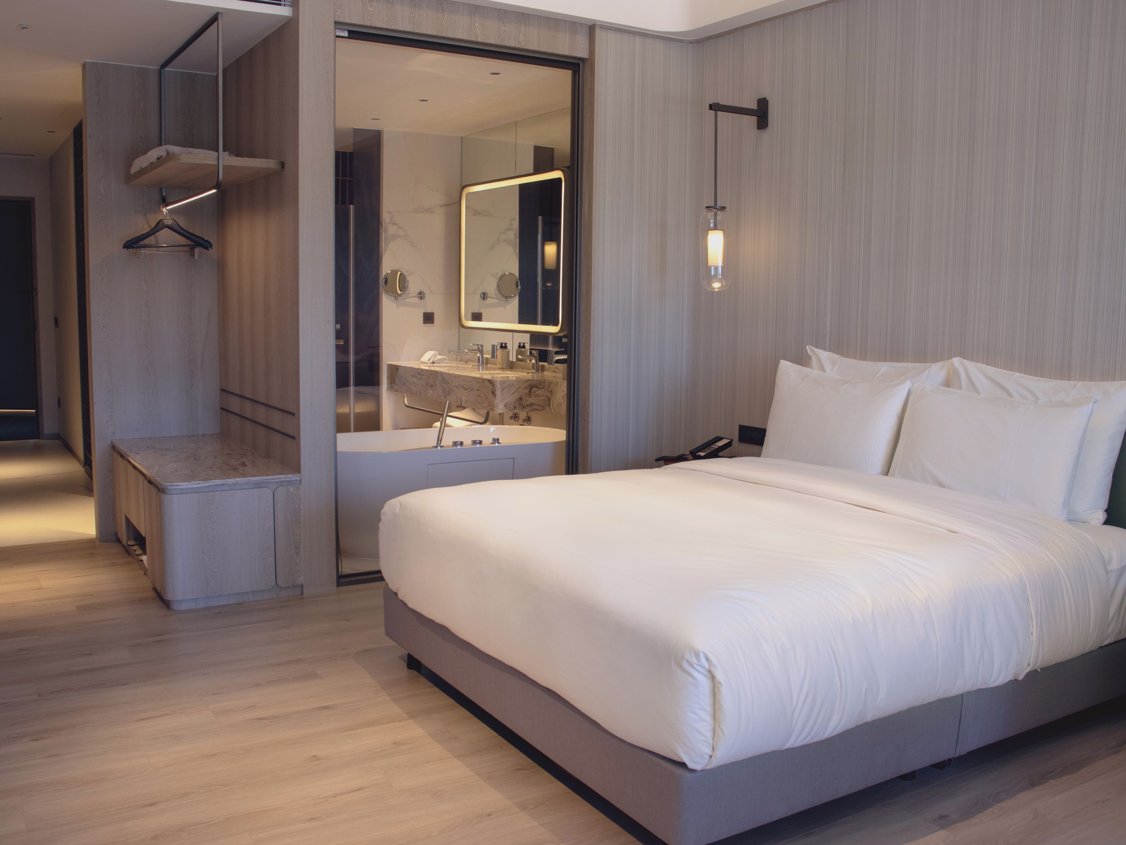 A modern hotel room with a large bed, a built-in vanity with a mirror, and a wooden floor.