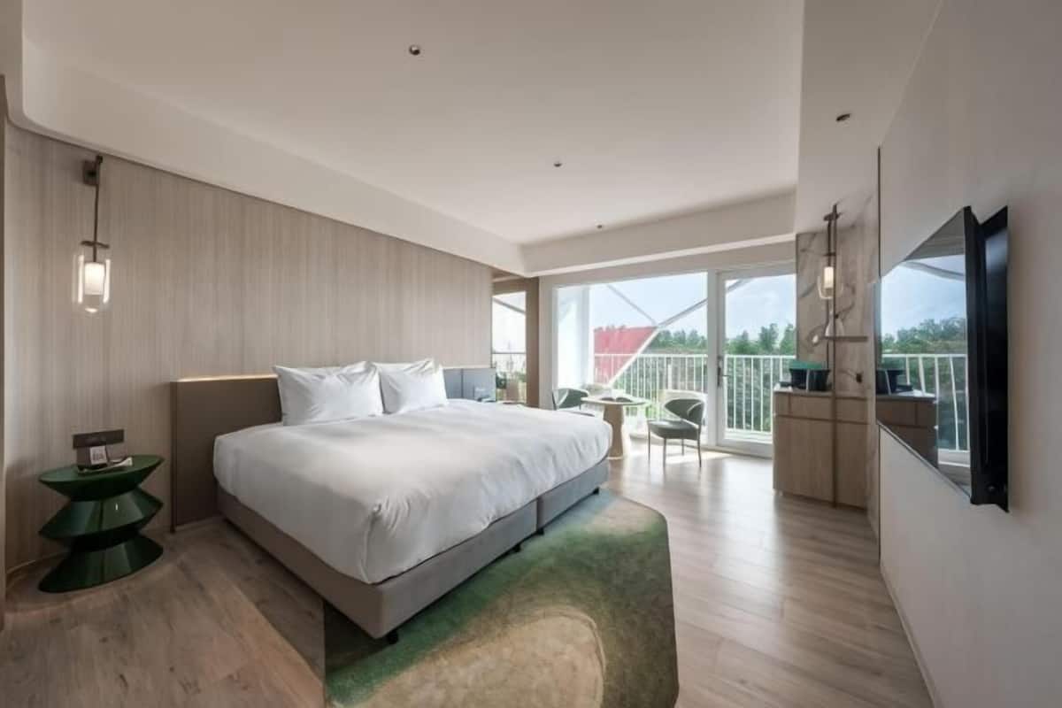 A modern bedroom with a large bed, a small desk, and a balcony with a view.