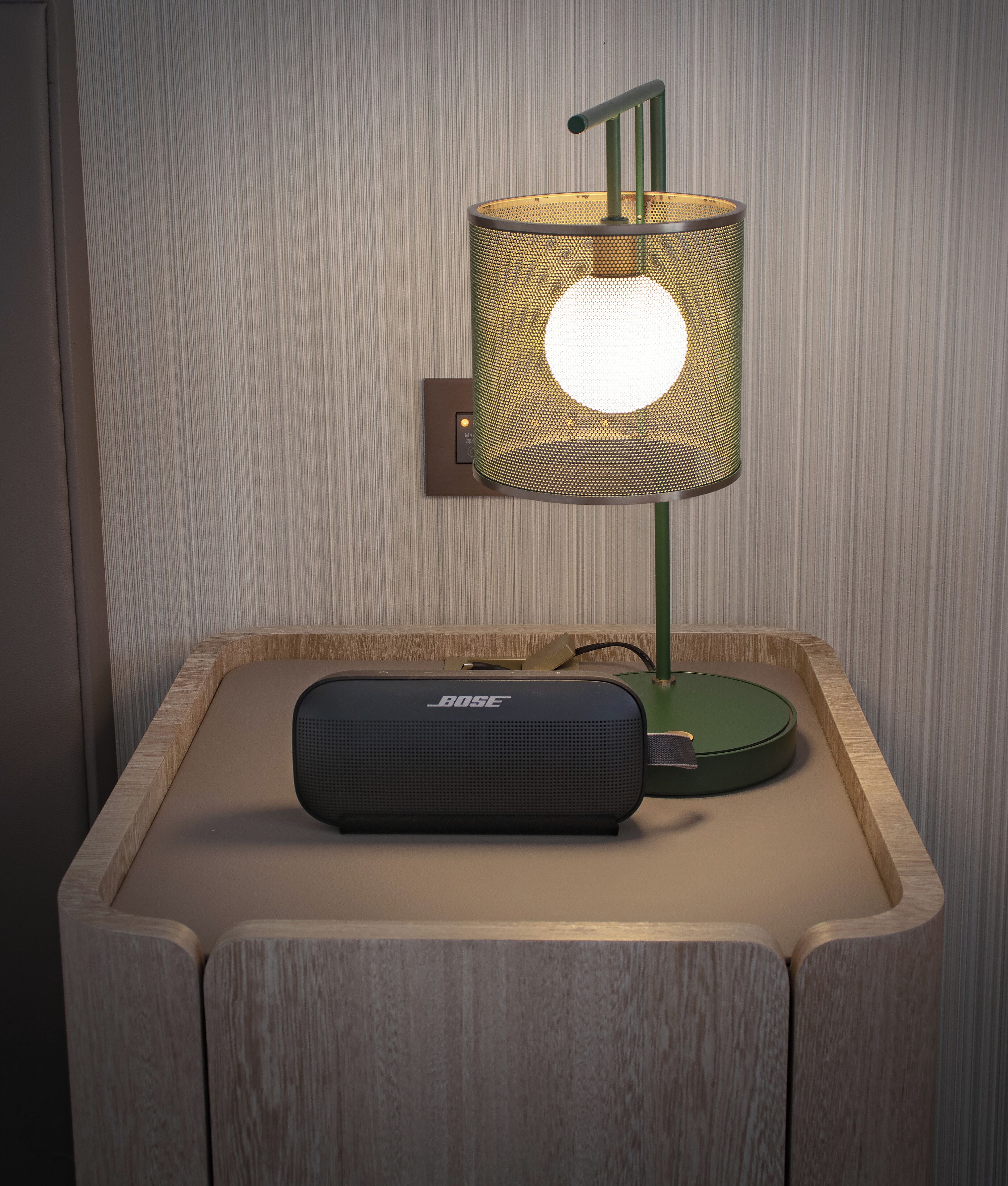 A bedside table with a green lamp and a black Bose speaker.