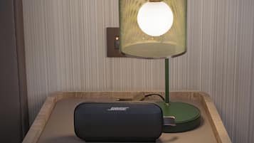 Een nachtkastje met een groene lamp en een zwarte Bose speaker.