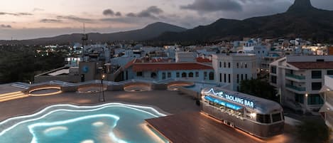 Una piscina en la azotea con un bar llamado Taolang Bar, rodeada de edificios y una montaña al fondo.