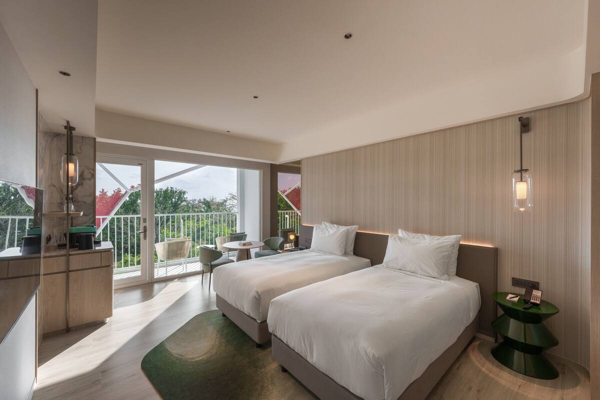 A modern hotel room with two beds, a balcony, a desk, and a small seating area.