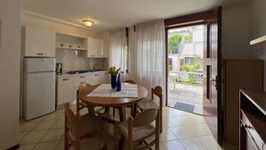 A compact kitchen with white cabinets, a refrigerator, and a dining table with chairs. There is a window with curtains and a view of a balcony. - Beautiful apartment for 5 guests with A/C, WIFI, TV, patio and pets allowed (Lignano Sabbiadoro)