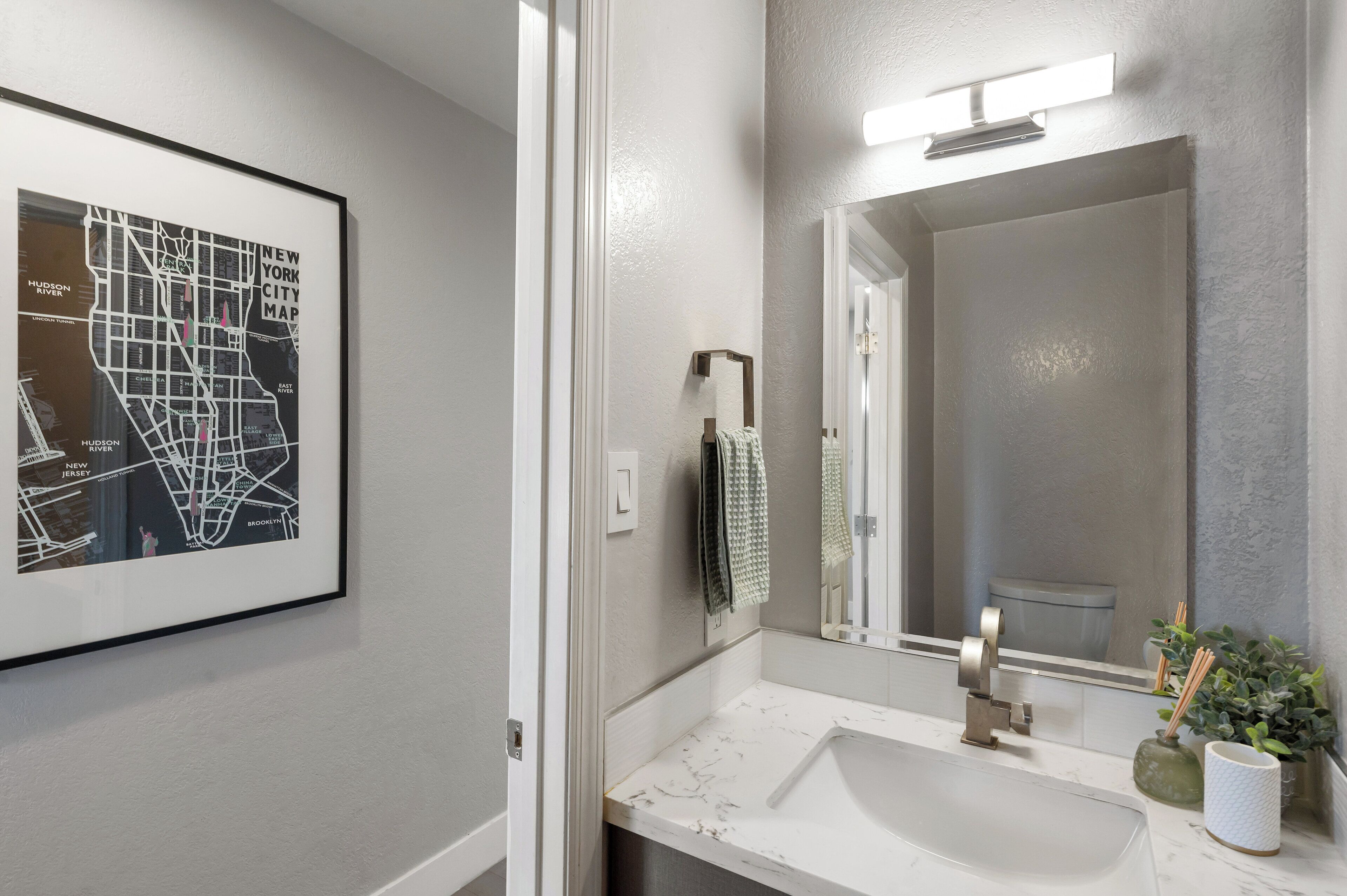 Une salle de bain avec un lavabo blanc, un grand miroir et une carte encadrée accrochée au mur.