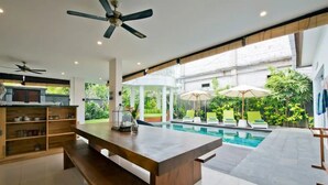 A spacious indoor area with a pool, a wooden table, and a ceiling fan. - 6BR Del Mar Villas W/2 Pool near Seminyak Beach (Seminyak)
