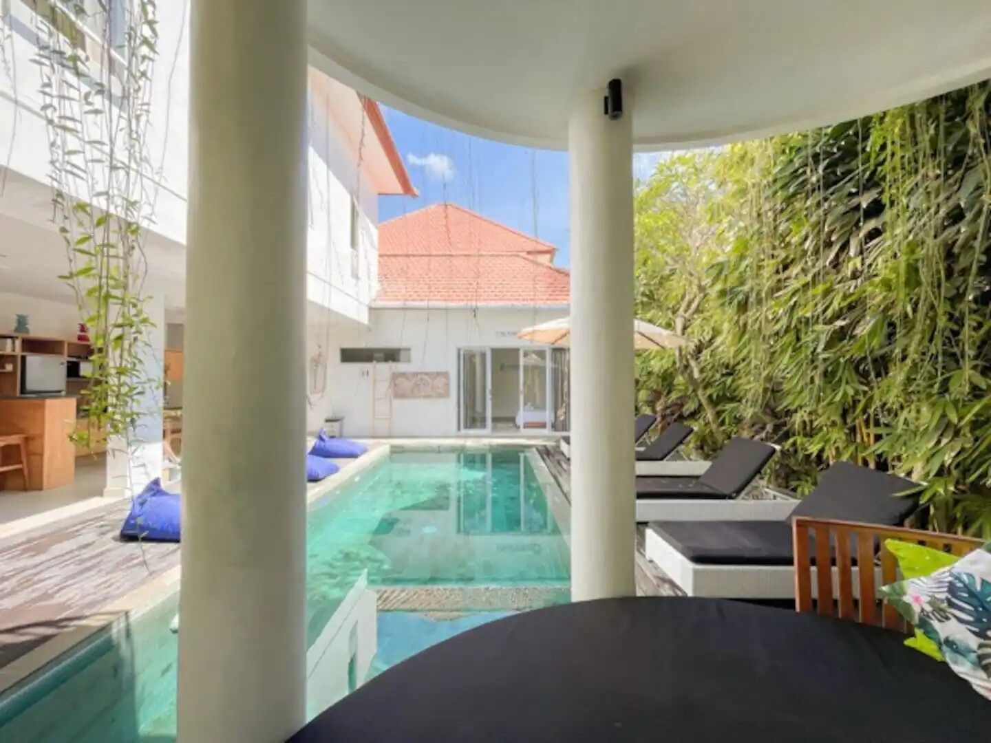 A poolside area with a clear view of a swimming pool, lounge chairs, and a building with a red roof in the background.