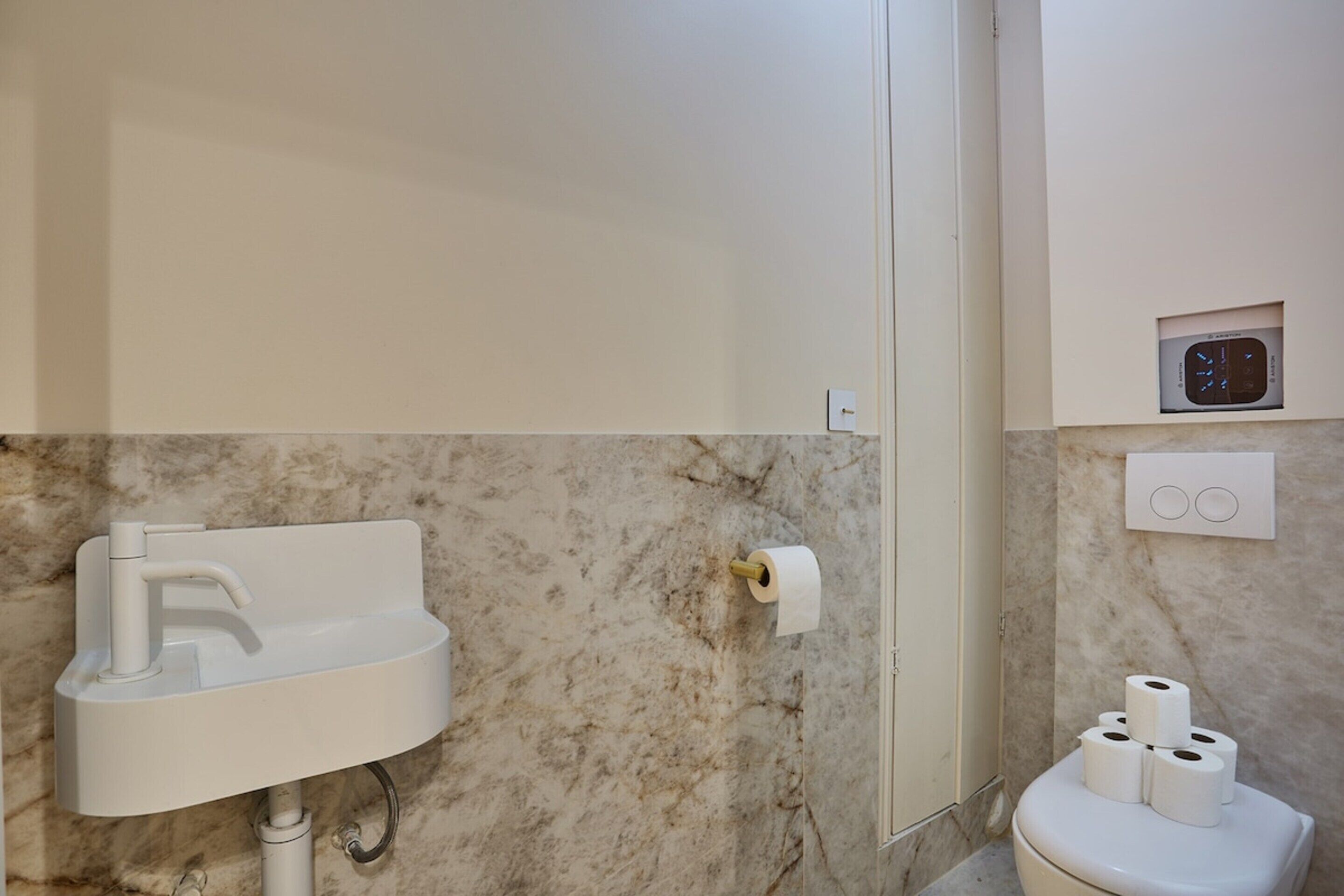 A bathroom with a marble sink, a toilet with toilet paper, and a wall-mounted clock.