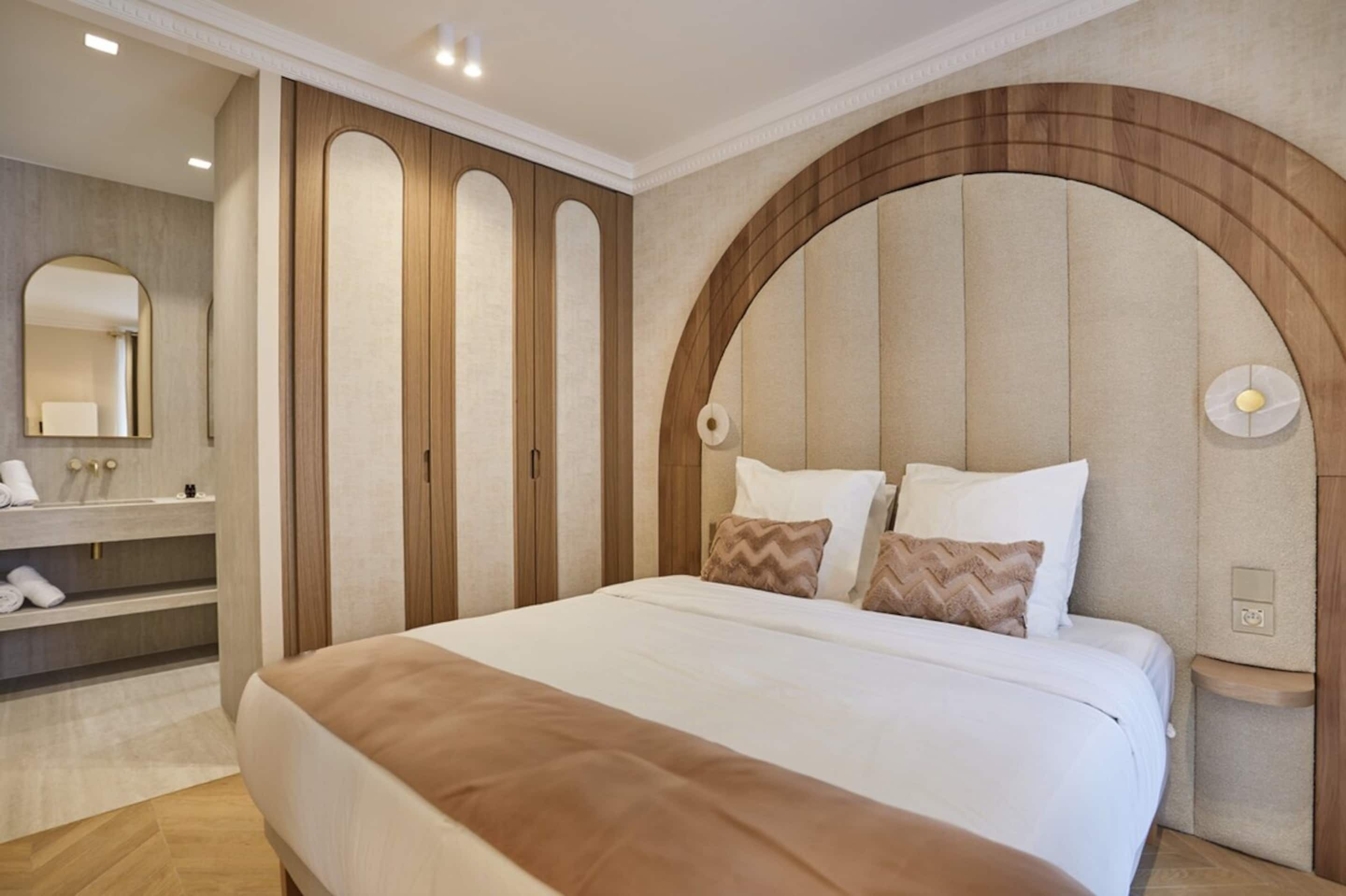Un dormitorio con una cama grande, una tocador empotrado con espejo y una original cabecera en arco.