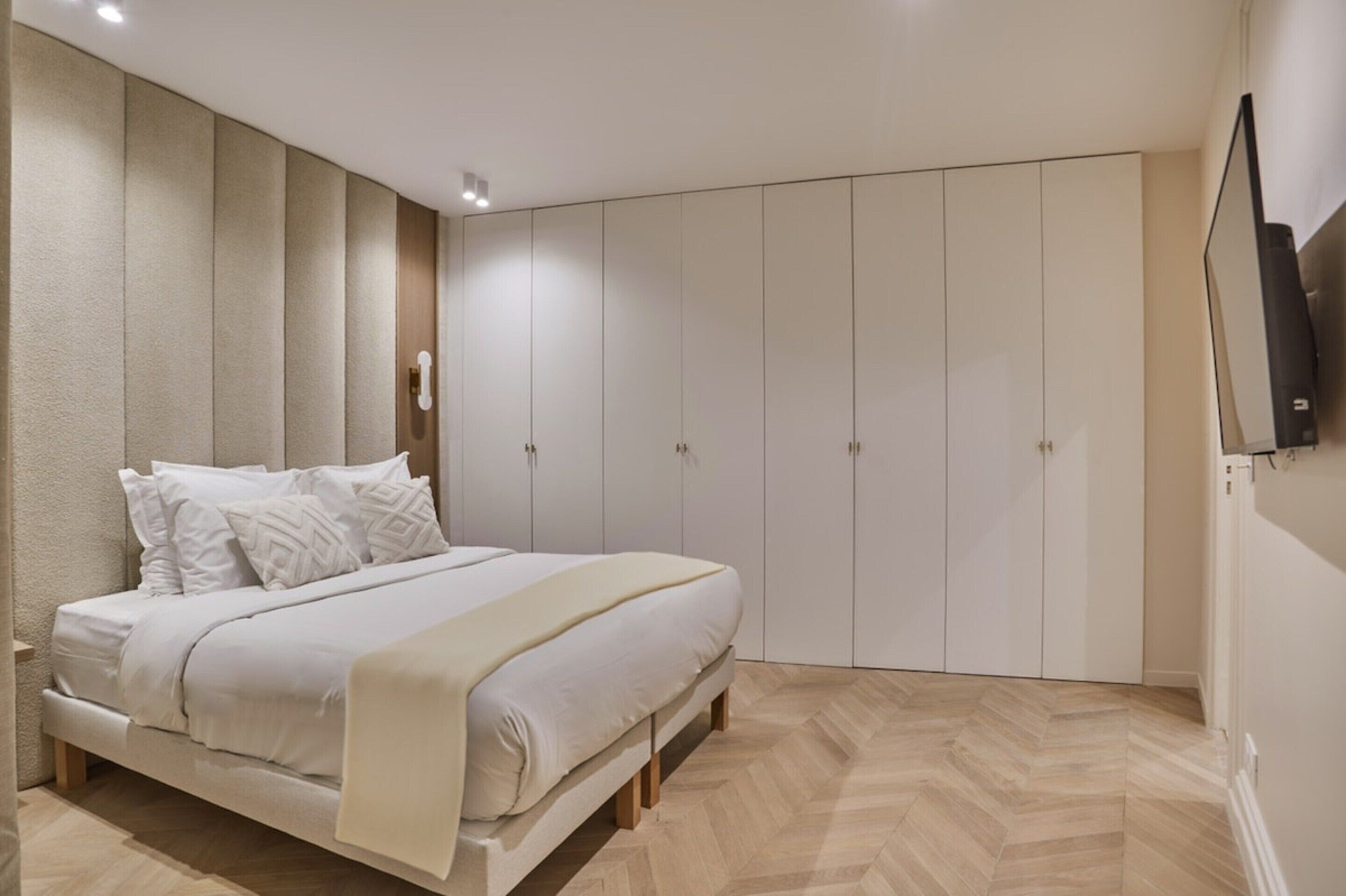 A bedroom with a bed, a wardrobe, and a television on the wall.