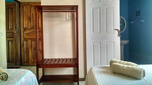 Una habitación con estructura de cama de madera, un banco, una puerta blanca y un baño visible a través de una puerta abierta.