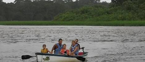 A family in a small boat on a calm body of water with dense greenery in the background.