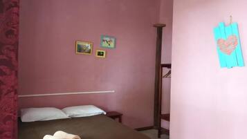 Un dormitorio con cama, una mesita de noche de madera, una lámpara colgante y una decoración con forma de corazón en la pared.
