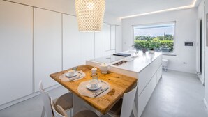 A modern kitchen with a wooden dining table, white cabinetry, and a large window offering a view of greenery. - Villa Il Guscio by Interhome (Terranuova Bracciolini)