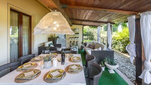 An outdoor patio with a wooden ceiling, wicker furniture, and a table set for dining. - Villa Il Guscio by Interhome (Terranuova Bracciolini)