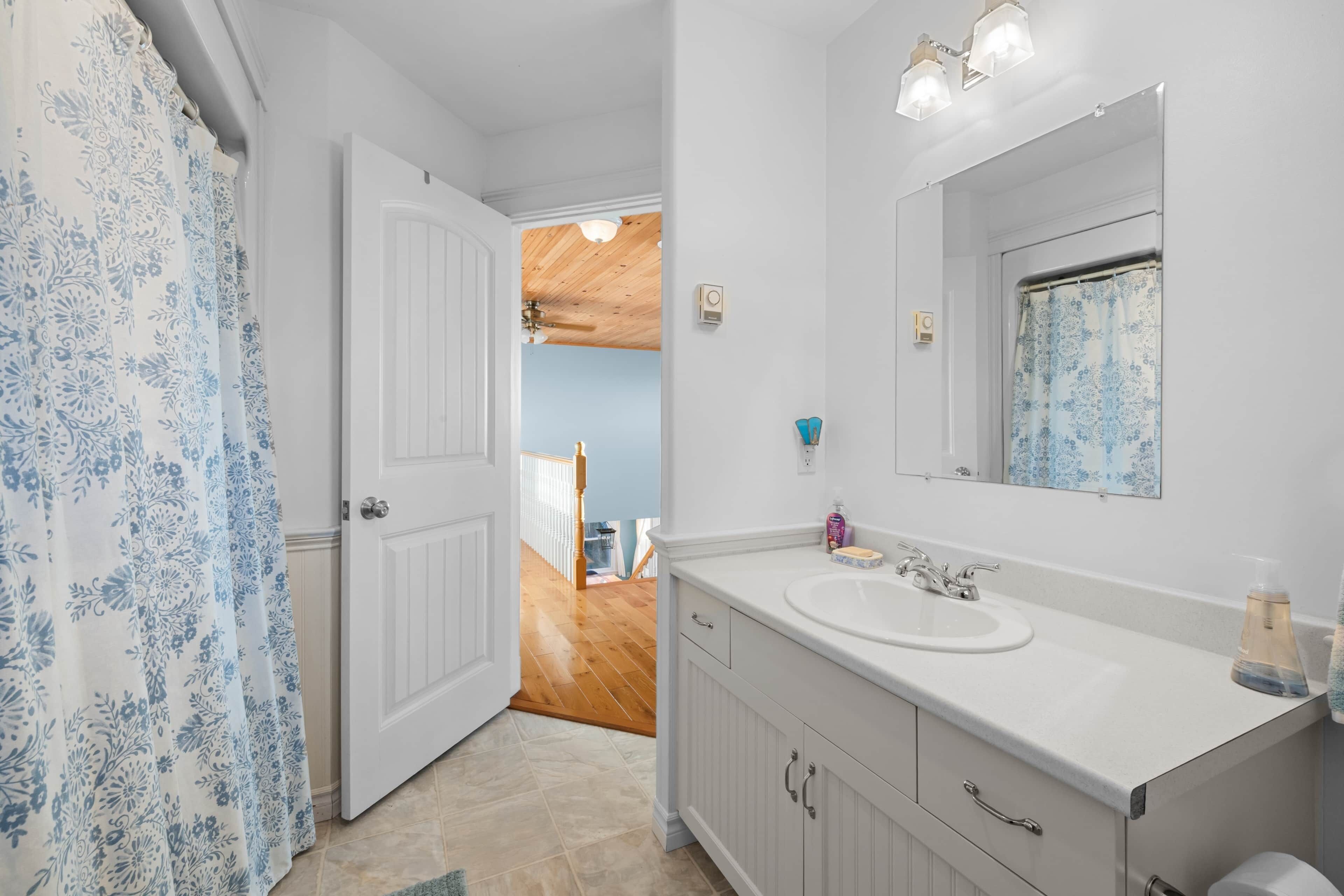 A bathroom with a white sink, mirror, and cabinets. There is a shower curtain with a blue floral pattern.