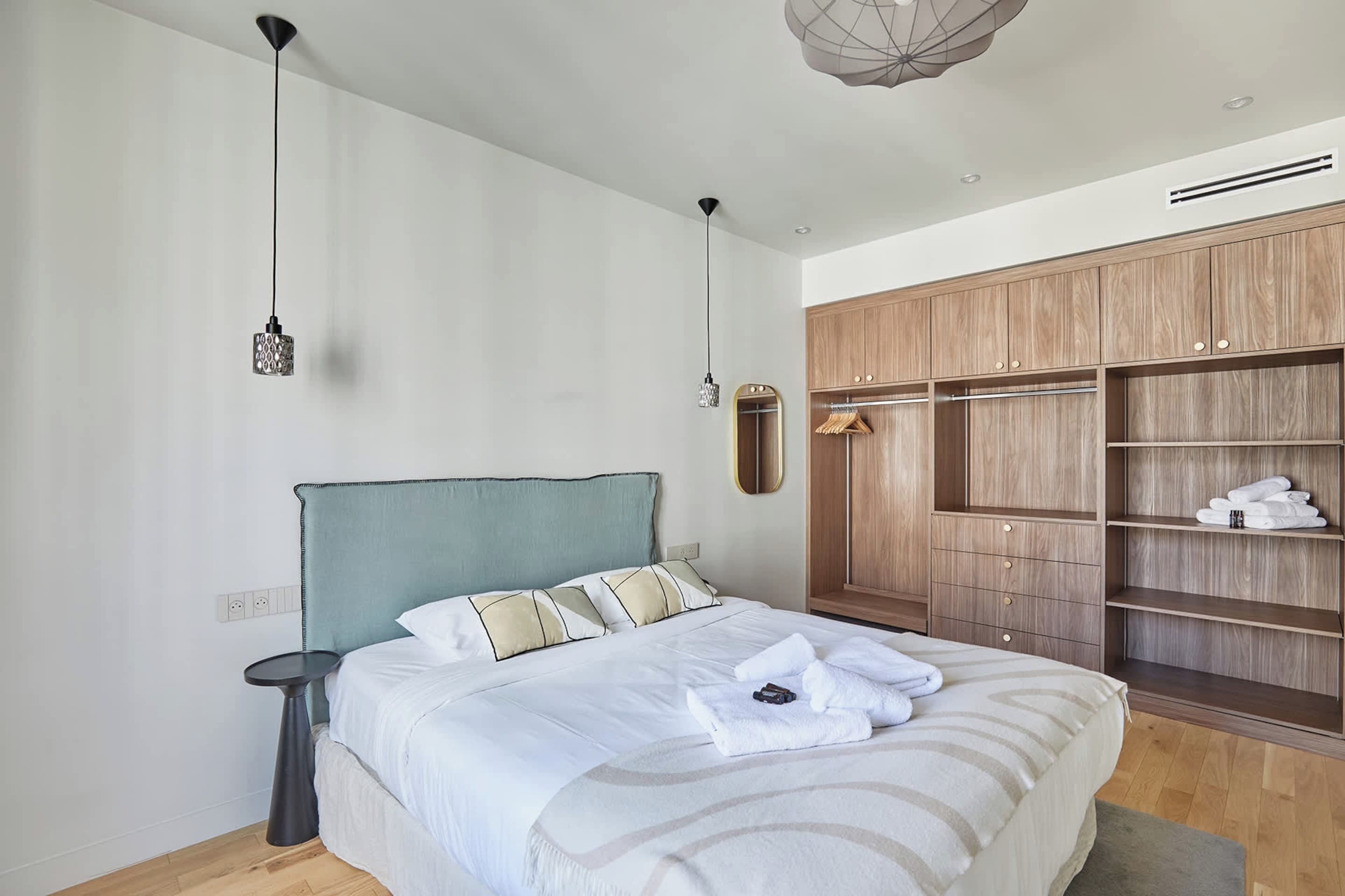 Un dormitorio con cama, mesita de noche, lámpara colgante, armario y espejo.