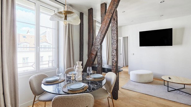 Ein Essbereich mit einem runden Tisch, Stühlen und einem an der Wand befestigten Fernseher.