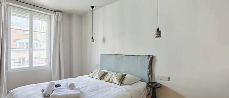 A neatly made bed with a striped blanket, a bedside table with a lamp, and a window with curtains.