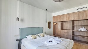 Ein ordentlich bezogenes Bett mit weißen Leinen, ein Nachttisch, ein Kleiderschrank mit Platz zum Aufhängen und Pendelleuchten.