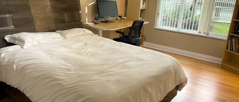 A bedroom with a large bed, a desk with a computer, a chair, and a bookshelf.