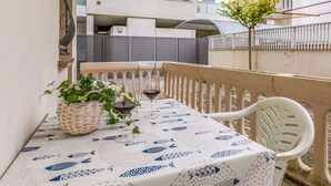 A balcony with a table set for two, featuring a tablecloth with a fish pattern, two glasses of red wine, and a woven basket with green plants. - Lovely apartment for 5 guests with A/C, WIFI, TV, terrace and pets allowed (Lignano Sabbiadoro)