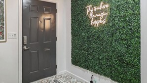 Een kamer met een donker houten deur, een groene wand met een neonbord en een kamerbreed tapijt met patroon.