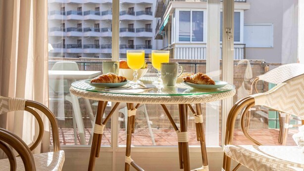 A balcony with a table set for breakfast, including croissants, orange juice, and a coffee mug.