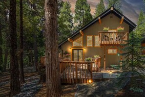A cabin with a wooden deck, a balcony with potted plants, and a large window. - Arnold’s Cozy Cabin  – Rustic-Modern Retreat Near Big Trees & Bear Valley (Arnold)
