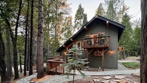 Une cabane dotée d’une terrasse en bois et d’un balcon, entourée d’une forêt.
