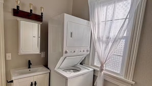 Ein Waschraum mit Waschmaschine und Trockner, einem Waschbecken und einem Fenster mit durchscheinenden Vorhängen.