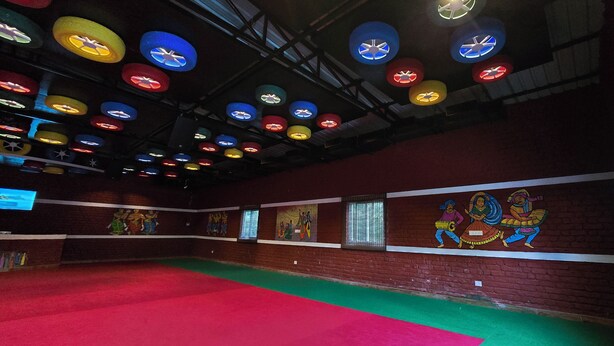 Um espaço interno amplo, com carpete vermelho, luminárias de teto coloridas e murais nas paredes.