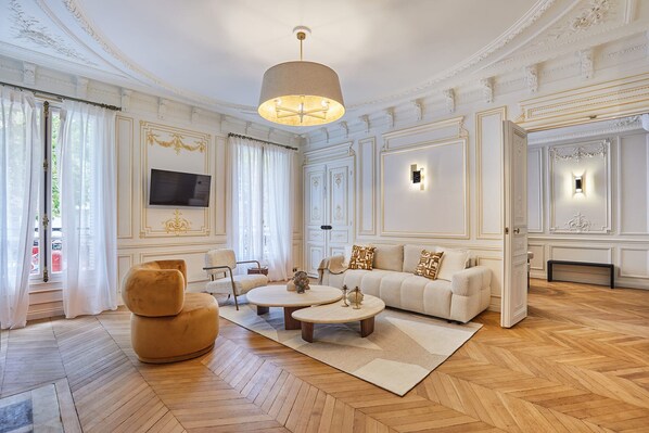 A spacious living room with a large sofa, two coffee tables, and a television mounted on the wall. - Amazing Apartment Saint Germain des Pres With AC by Studio Prestige (Paris)