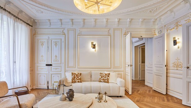 A spacious living room with a large sofa, two coffee tables, and a chandelier.