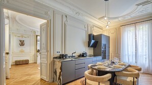 A spacious kitchen with marble countertops, a central island, and modern appliances. There is a dining area with a round table and chairs.