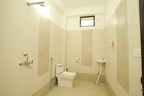 Une petite salle de bain bien éclairée, équipée de toilettes, d’un lavabo et d’une douche.