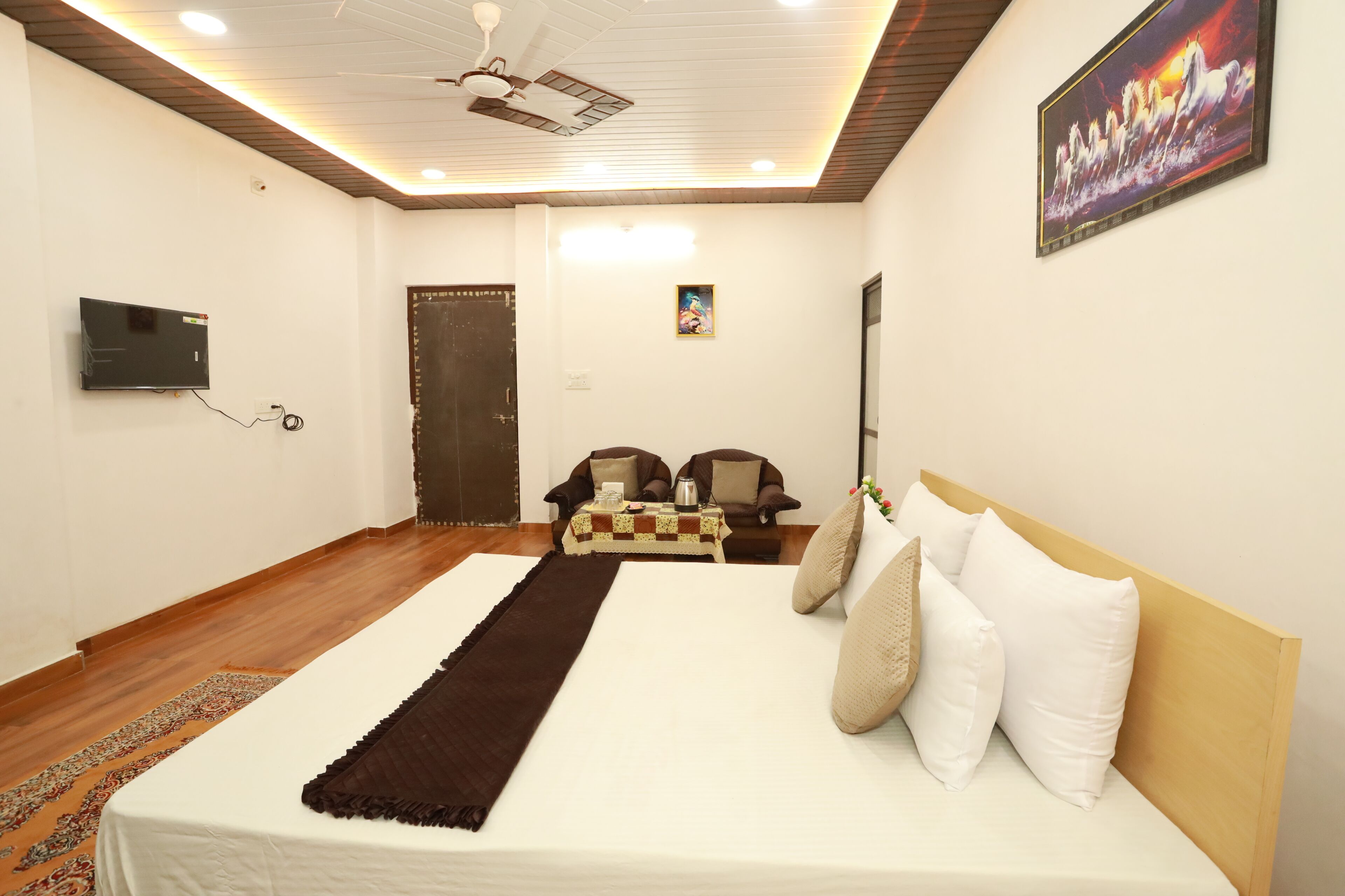 A bedroom with a large bed, a ceiling fan, a TV mounted on the wall, and a door in the background.