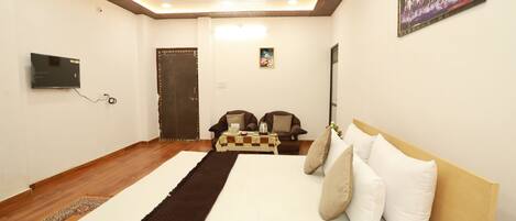 A bedroom with a large bed, a ceiling fan, a TV mounted on the wall, and a door in the background.