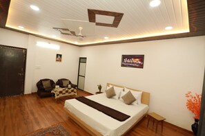 Une chambre moderne avec un grand lit, un bureau, deux chaises, un ventilateur de plafond et un téléviseur.