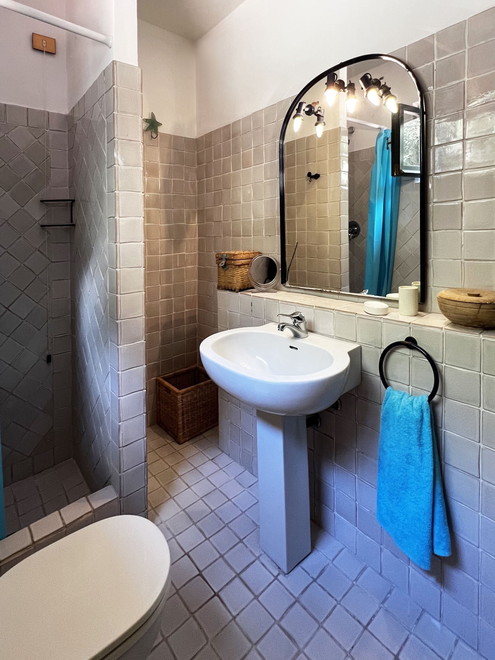 Une salle de bain avec un lavabo blanc, un miroir, une serviette bleue et un espace douche.