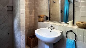 Une salle de bain avec un lavabo blanc, un miroir, une serviette bleue et un espace douche.