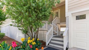 A residential house with a front porch, a staircase leading to the garage, and a variety of colorful flowers in the front yard. - Pet Friendly | Spacious Kitchen | Wine Fridge | Garage | Decks | Bonus Room | Fenced Backyard (St. Simons Island)