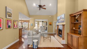 A spacious living room with hardwood floors, a ceiling fan, a fireplace, and a dining area in the background. - Pet Friendly | Spacious Kitchen | Wine Fridge | Garage | Decks | Bonus Room | Fenced Backyard (St. Simons Island)