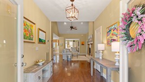 A hallway with wooden flooring, a ceiling fan, and wall-mounted artwork. - Pet Friendly | Spacious Kitchen | Wine Fridge | Garage | Decks | Bonus Room | Fenced Backyard (St. Simons Island)