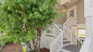 A staircase with white railings leading to a door, surrounded by greenery and yellow flowers. - Pet Friendly | Spacious Kitchen | Wine Fridge | Garage | Decks | Bonus Room | Fenced Backyard (St. Simons Island)