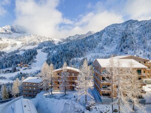 A snow-covered mountain resort with multi-story buildings, ski slopes, and dense forests.