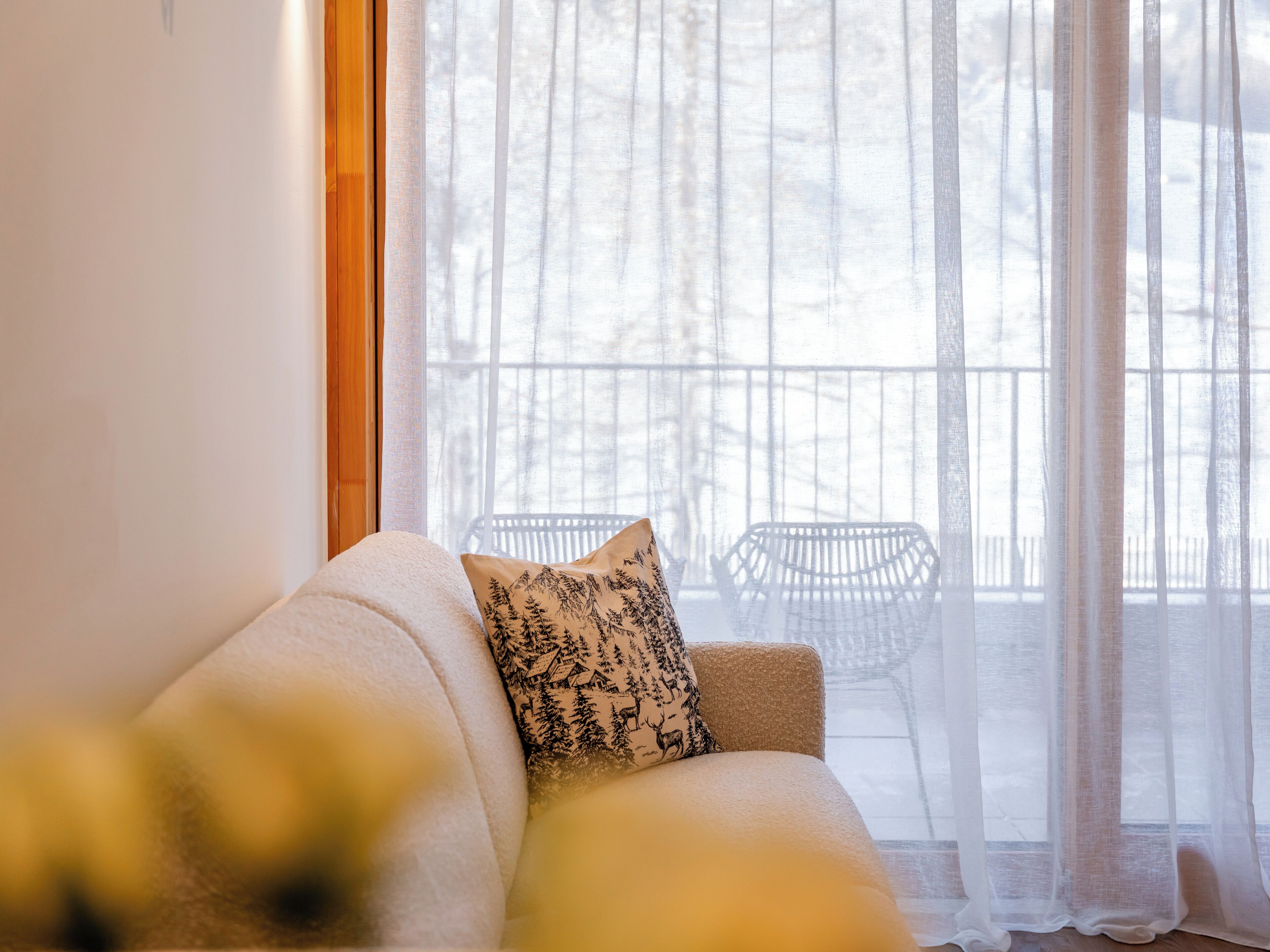 Ein gemütliches Wohnzimmer mit einer Couch und einem Fenster mit durchscheinenden Vorhängen.