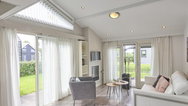 A modern living room with a grey sofa, a small round table, and a TV mounted on the wall. - Nice house in Zeeland near the Oosterschelde (Kattendijke)