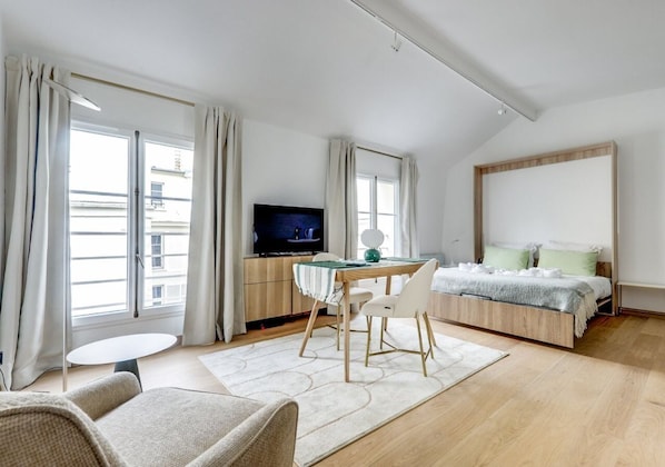 Een moderne hotelkamer met een bed, een televisie, een eettafel en een bank.